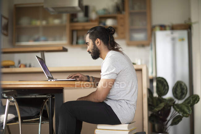 Чоловік сидить на стопі книг, використовуючи свій ноутбук — стокове фото