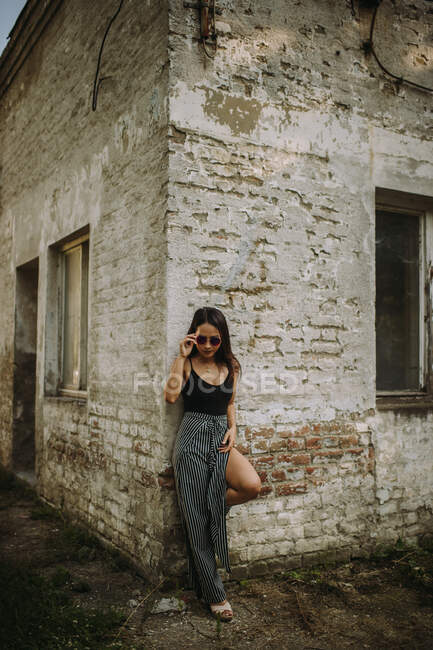 Giovane donna elegante in occhiali da sole in posa da muro vecchio edificio — Foto stock