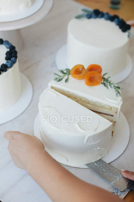 Woman cutting cake with buttercream icing and peaches — Stock Photo