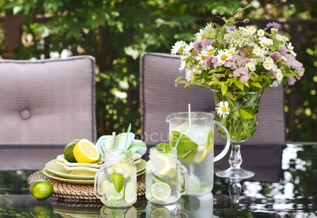 Limonata in brocca e tazze sul tavolo in giardino. — Foto stock