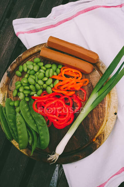 Vista elevada de frijoles lima, cebolla de primavera, tofu, mangetout y pimientos en una tabla de cortar - foto de stock