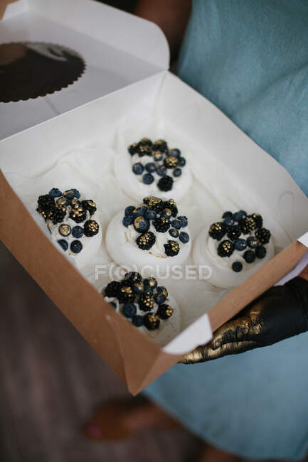 Woman holding a box of mini Pavlova desserts with blueberries and blackberries — Stock Photo