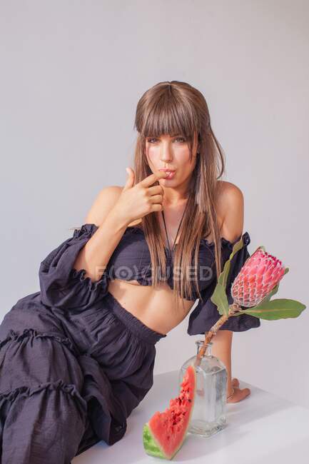 Portrait of a woman sitting next to a vase and slice of watermelon with her finger on her mouth — Stock Photo