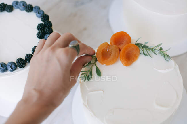 Donna che decora una torta con glassa al burro e pesche — Foto stock