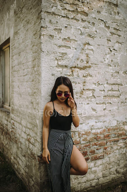 Young stylish woman in sunglasses posing by old building wall — Stock Photo
