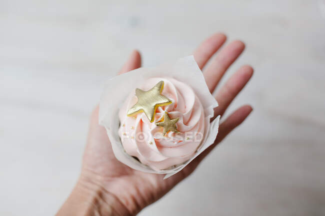 Woman's hand holding a cupcake with buttercream icing and gold colored decoration — Stock Photo
