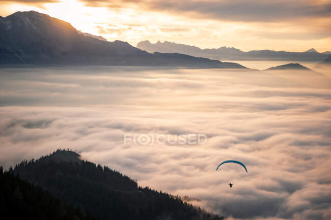 Distant view of person flying on parachute in mountainous landscape with low clouds — Stock Photo