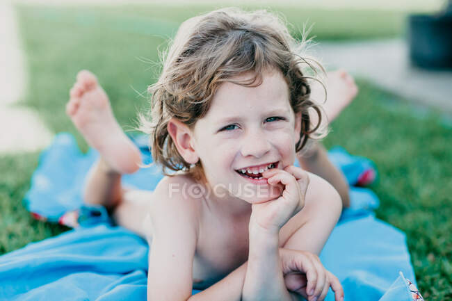 Sonriente niño acostado sobre una manta en el jardín - foto de stock