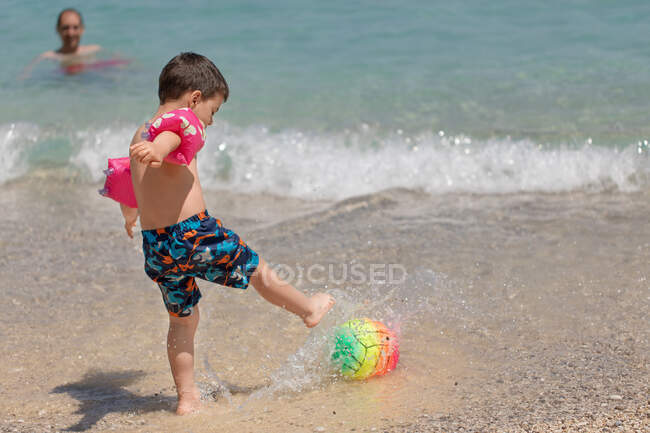 Padre e hijo jugando con una pelota de playa en el océano, Grecia - foto de stock