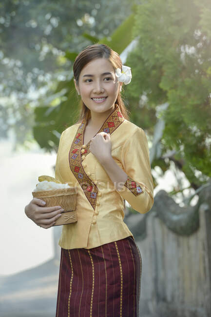 Mujer vestida con un traje tradicional de Laos llevando un tazón de arroz, Laos - foto de stock