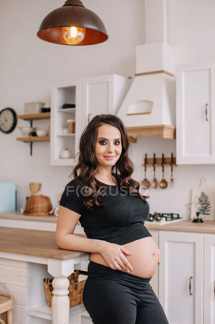 Улыбающаяся беременная женщина стоит на кухне — стоковое фото