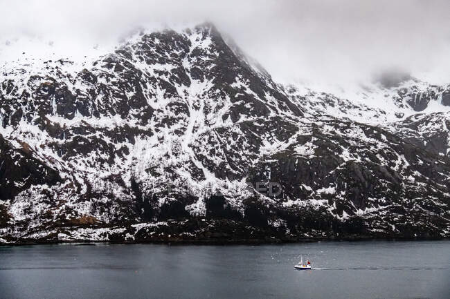 Boot segelt an einem schneebedeckten Berg vorbei, Lofoten, Nordland, Norwegen — Stockfoto