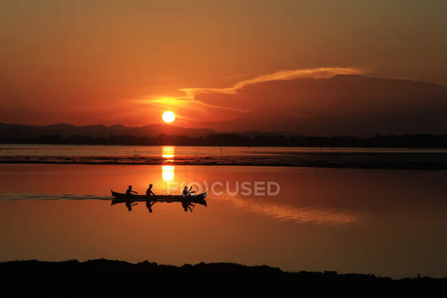Coucher de soleil reflétant dans le lac avec des silhouettes de personnes sur le bateau, lac de Limboto, Gorontalo, Indonésie — Photo de stock