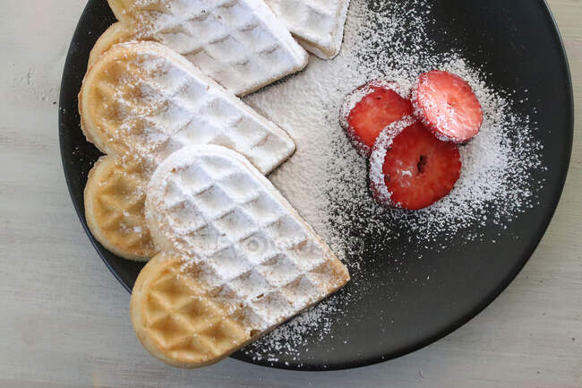 Close-up of heart shaped waffles decorated with icing sugar and strawberries — Stock Photo