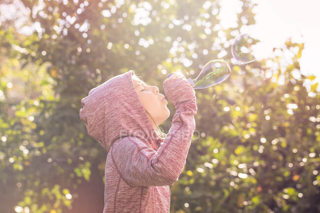 Menino de pé no jardim e soprando bolhas de sabão — Fotografia de Stock