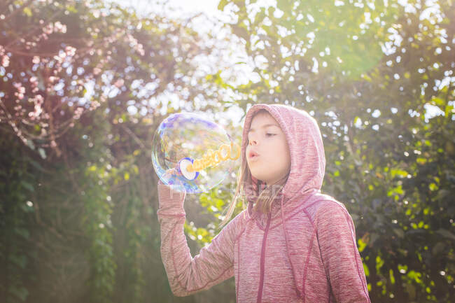 Niño de pie en el jardín y soplando burbujas de jabón - foto de stock