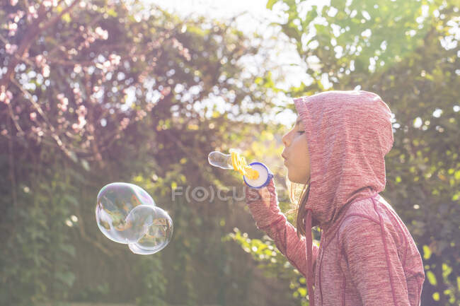 Menino de pé no jardim e soprando bolhas de sabão — Fotografia de Stock