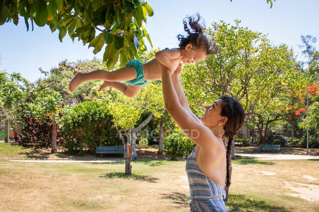 Жінка стоїть у парку і кидає свою дочку в повітря (Бразилія). — стокове фото