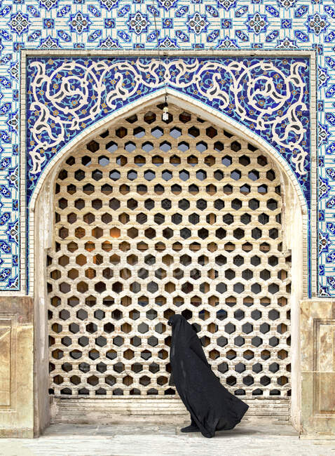 Mujer vestida con una abaya negra caminando junto a una mezquita, Irán - foto de stock
