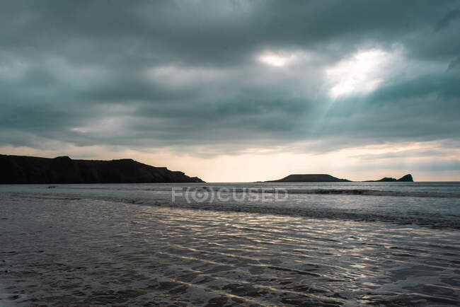 Nubes de lluvia sobre Worms Head y Rhossili Bay, Gales, Reino Unido - foto de stock