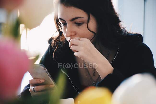 Adolescente sentada em uma mesa usando um telefone celular — Fotografia de Stock