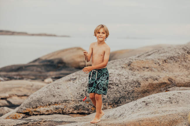 Niño de pie en las rocas de pesca de cangrejos, Verdens Ende, Tjome, Tonsberg, Noruega - foto de stock