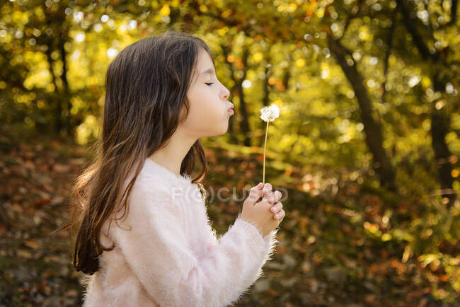 Girl standing outdoors blowing a dandelion, Bulgaria — Stock Photo