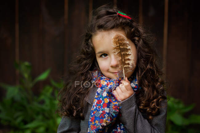 Chica sonriente sosteniendo una pluma delante de su cara - foto de stock