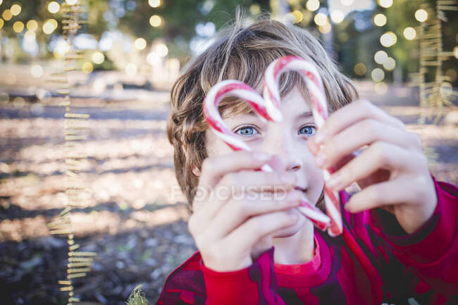 Garçon debout dans le jardin faisant une forme de coeur avec deux cannes à bonbons, Espagne — Photo de stock