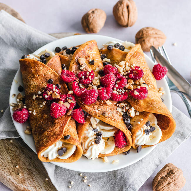 Pumpkin crepes with whipped cream, banana, nuts and raspberries — Stock Photo