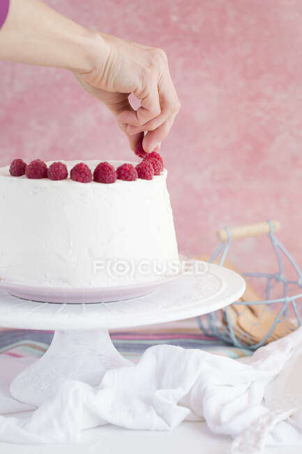 Female hand decorating raspberry cream cake on cake stand, close view — Stock Photo