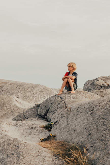 Niño sentado en las rocas, Verdens Ende, Tjome, Tonsberg, Noruega - foto de stock