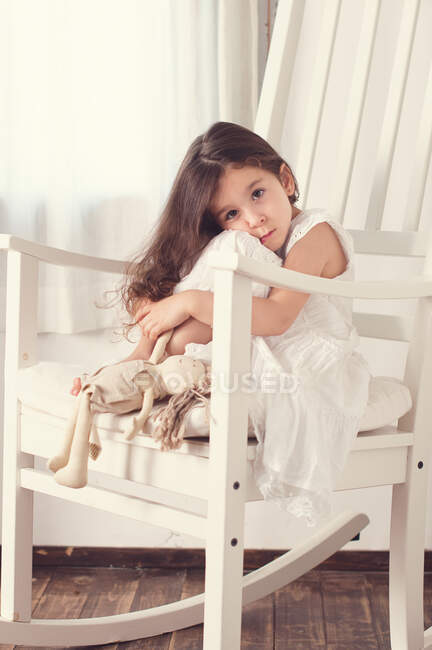 Menina sentada em uma cadeira de balanço com uma boneca — Fotografia de Stock