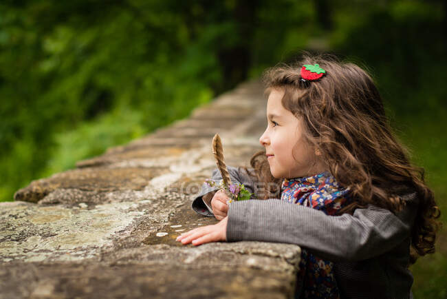 Girl standing by a wall holding a feather — Stock Photo
