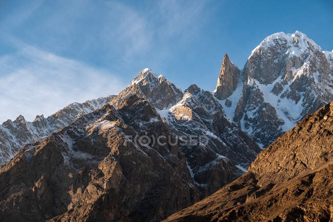 View of sun lighted and snowcapped rocks under blue cloudy sky — Stock Photo