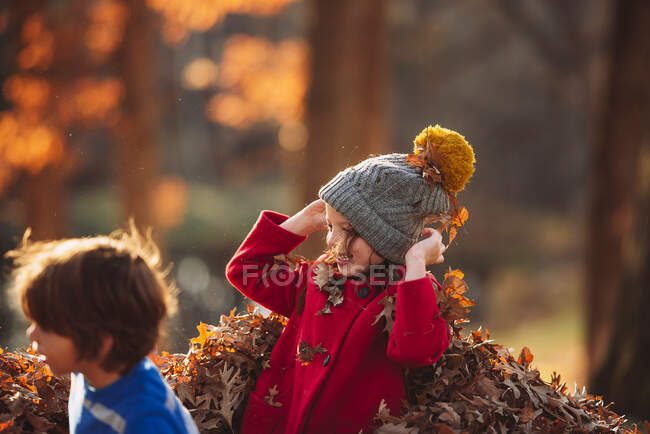 Garçon et fille jouant dans une pile de feuilles, États-Unis — Photo de stock