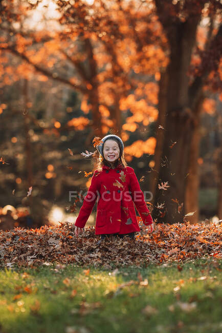Sorrindo menina jogando folhas de outono no ar, Estados Unidos — Fotografia de Stock