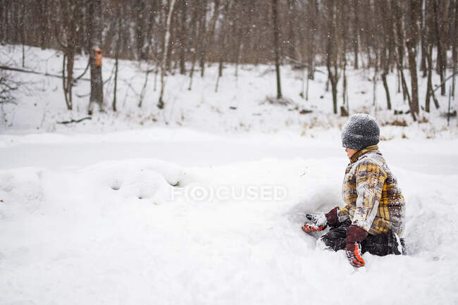 Мальчик в зимней одежде, покрытый снегом, играет со снегом в парке — стоковое фото