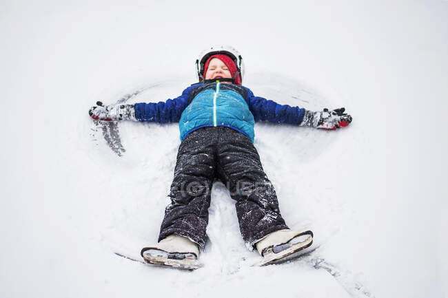 Niño acostado en la nieve haciendo un ángel de nieve, Wisconsin, Estados Unidos - foto de stock