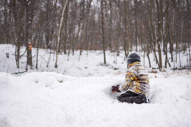 Boy in winter clothes covered in snow playing with snow in park scene — Stock Photo