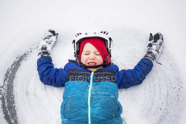 Niño acostado en el lago congelado haciendo un ángel de nieve, Wisconsin, Estados Unidos - foto de stock