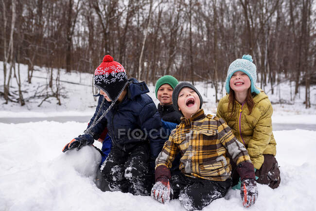 Four happy children on snow in winter forest scene — Stock Photo