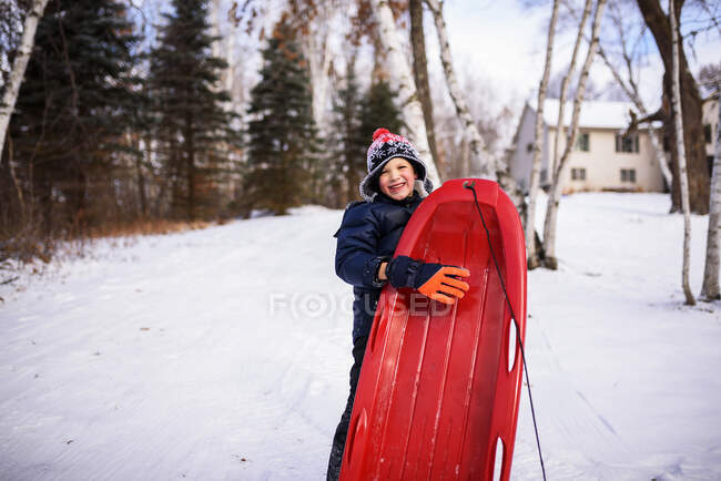 Junge steht mit seinem Schlitten in einem Garten, Wisconsin, Vereinigte Staaten — Stockfoto