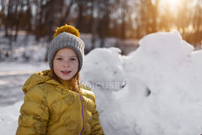 Retrato de una chica sonriente de pie junto a un fuerte de nieve, Estados Unidos - foto de stock