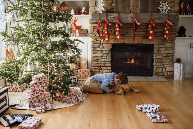 Garçon étreinte avec chien à Noël intérieur décoré — Photo de stock