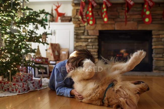 Мальчик обнимается с собакой в рождественском украшенном интерьере — стоковое фото