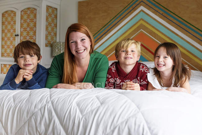 Madre y tres hijos acostados en la cama sonriendo - foto de stock