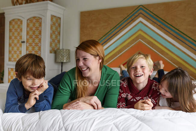 Мати і троє дітей лежать на ліжку посміхаючись — стокове фото