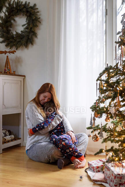 Mamma e figlio abbracciati dall'albero di Natale a casa — Foto stock