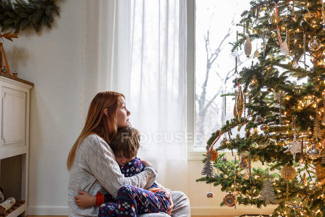 Mãe e filho abraçando pela árvore de natal em casa — Fotografia de Stock